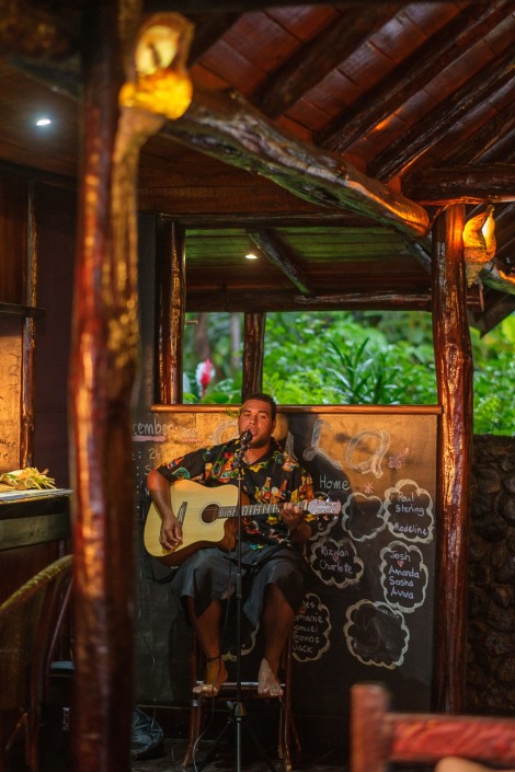 A seated man singing and playing acoustic guitar at resort bar in Fiji