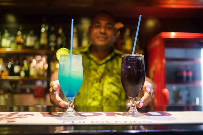 Fijian man serving two tropical cocktails from resort bar