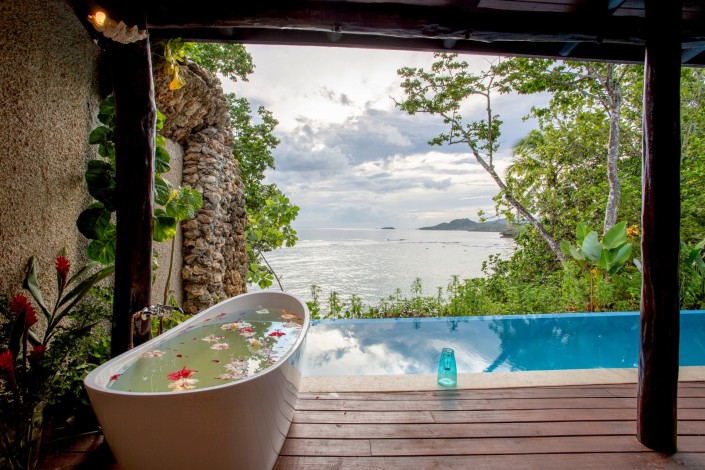 Tropical view of an outdoor bath filled with petals set beside a swimming pool overlooking the ocean