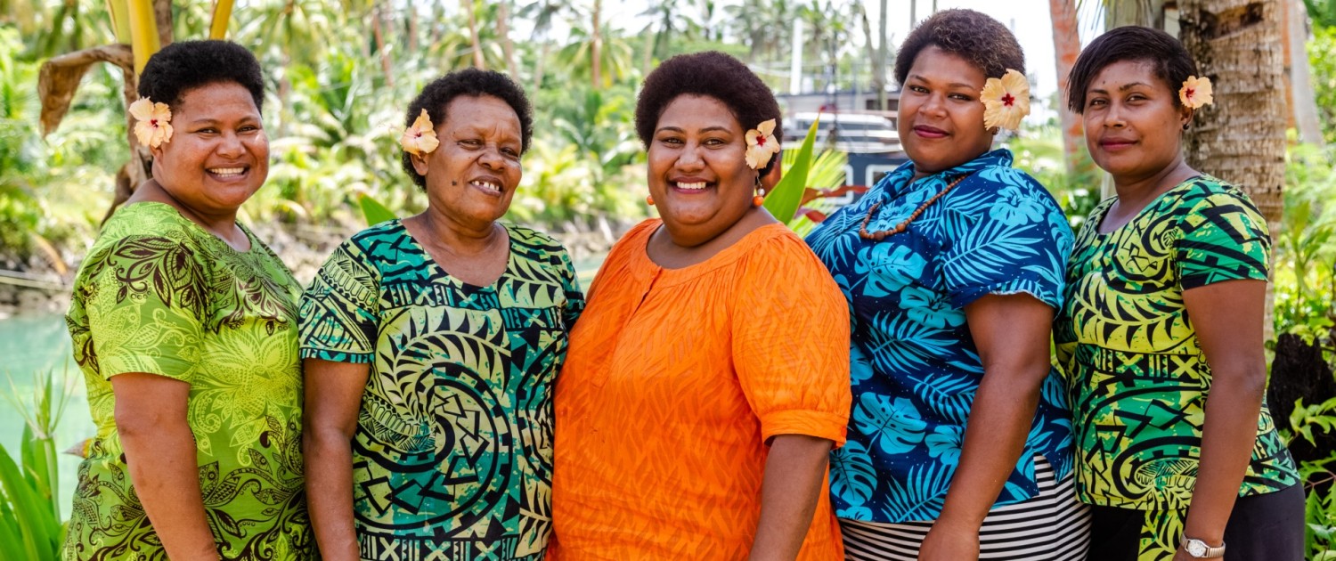Group of Fijian women smiling in brightly coloured clothing with flowers in their hair