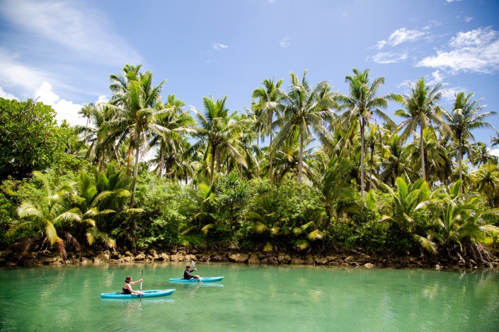 Holidaying couple paddleboarding in lagoon with backdrop of tropical palm trees
