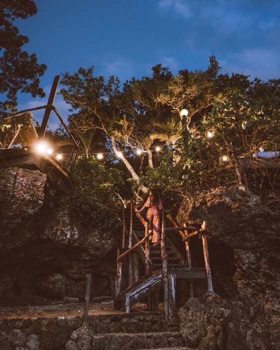 Woman walking up outdoor staircase at night with fairylights overhead