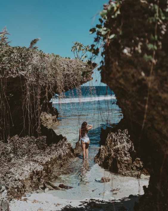 Woman walking into ocean amongst rugged limestone landscape in Savusavu Fiji