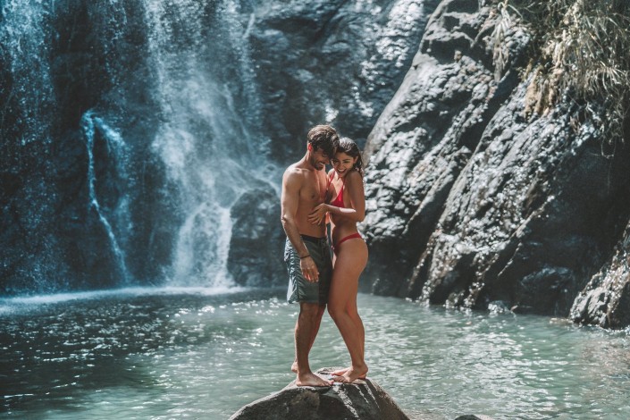 Young honeymoon couple smiling on a rock in front of a waterfall in Savusavu Fiji